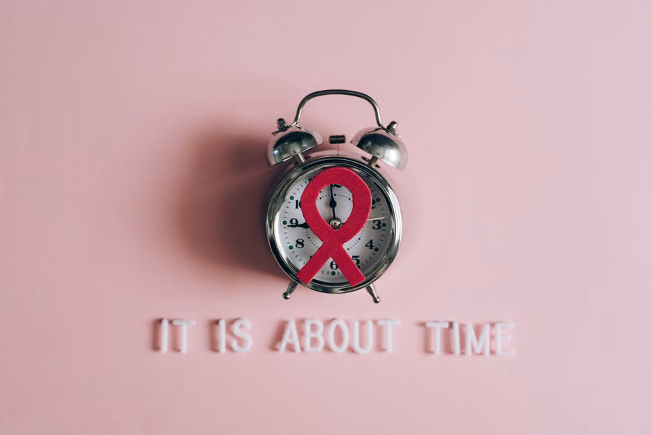Alarm clock featuring an AIDS awareness ribbon on a pink background, symbolizing urgency and awareness.